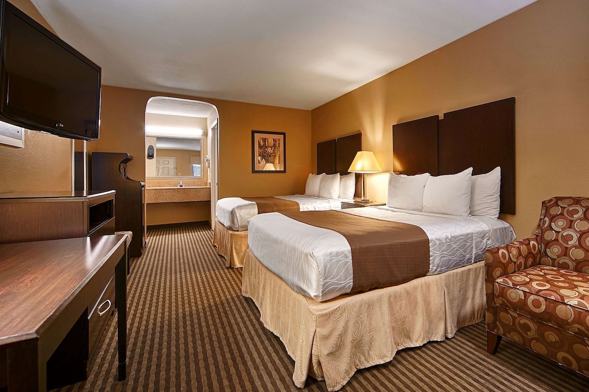 A hotel room with a bed, two bedside tables, a desk, a chair, a TV, and a mirror.