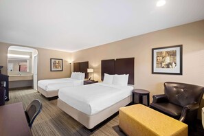 Une chambre d’hôtel avec deux lits, un bureau, une chaise, une petite table et un tableau encadré au mur.