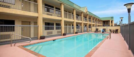 Un hotel con piscina, asientos al aire libre y un paseo techado.