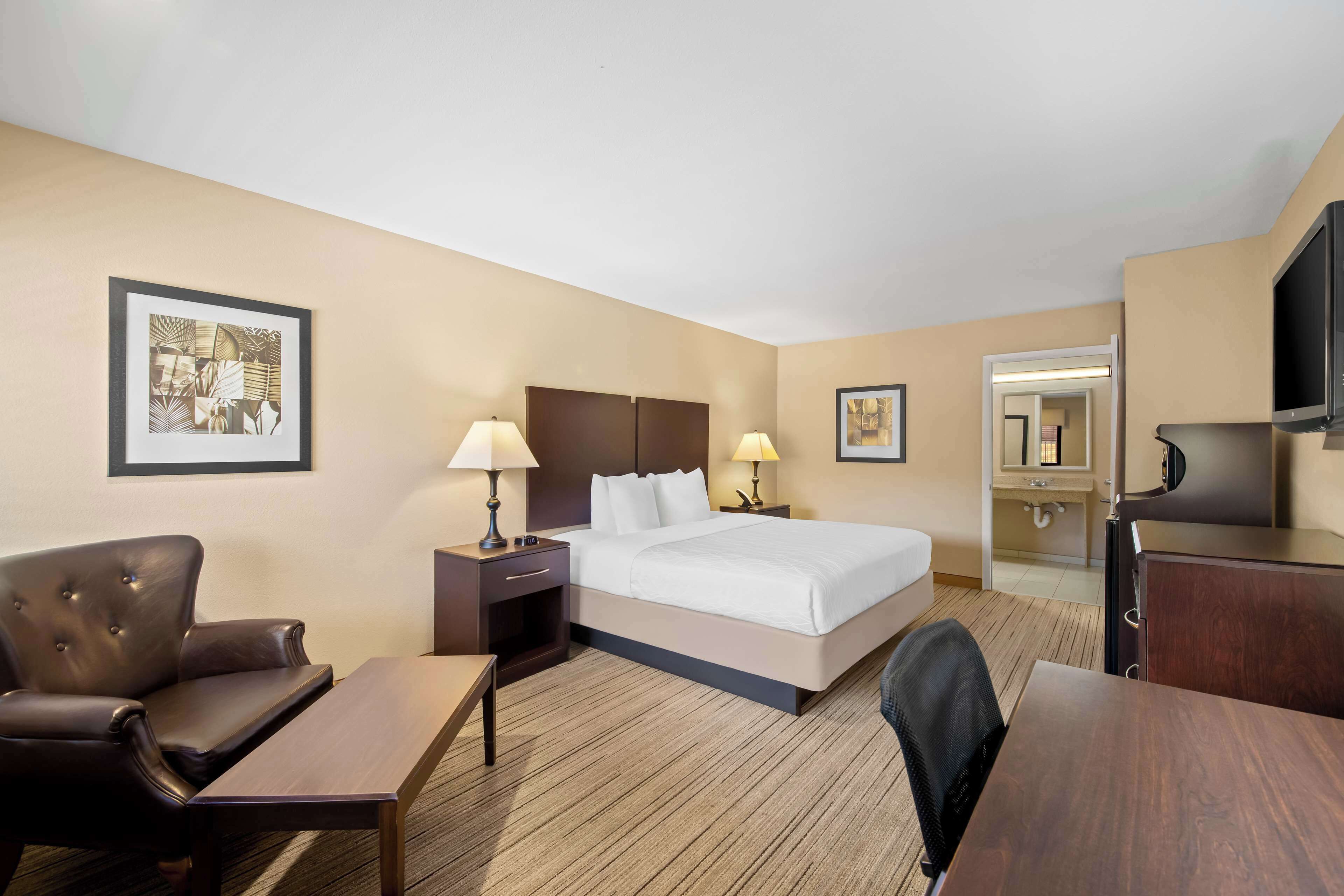Habitación de hotel con cama, escritorio, silla, televisión y baño visible a través de una puerta abierta.