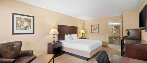 Habitación de hotel con cama, escritorio, silla, televisión y baño visible a través de una puerta abierta.