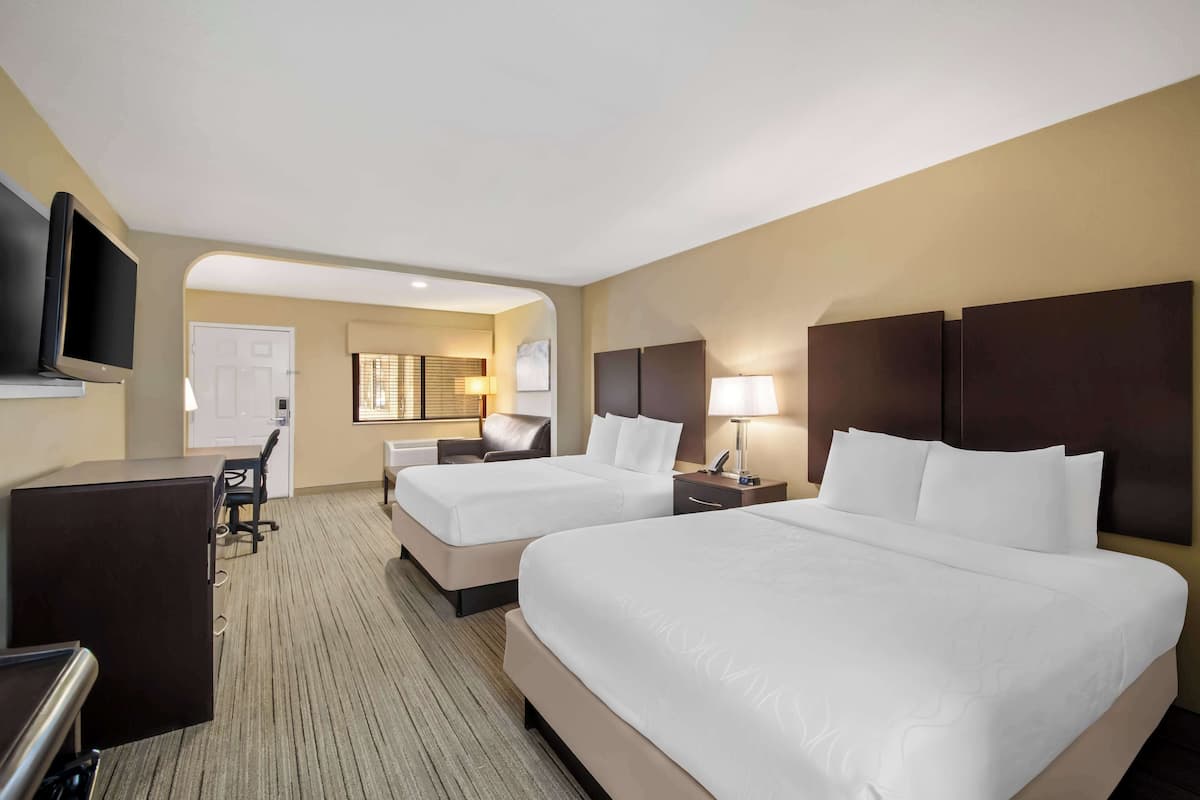 A hotel room with two beds, a desk, a TV, and a seating area.