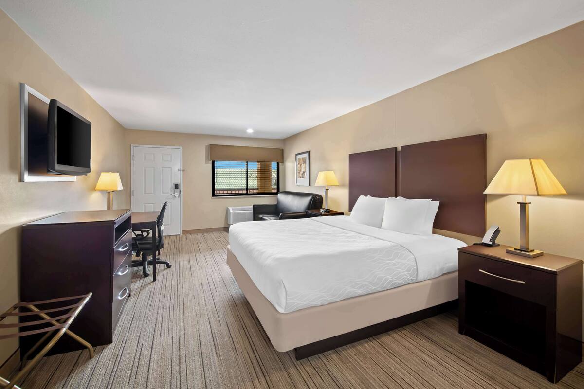 A hotel room with a large bed, desk, chair, TV, and two bedside lamps.