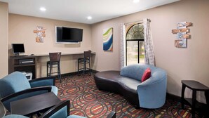 A hotel room with a curved sofa, a desk with a computer, a TV mounted on the wall, and a window with curtains. - Best Western Cedar Inn (Cedar Park)