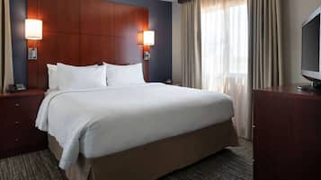 Una habitación de hotel con una cama grande, dos lámparas de noche, un televisor, un cabecero de madera, una mesita de noche y un escritorio.