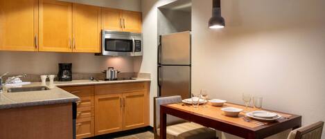 A modern kitchen with wooden cabinets, a stainless steel refrigerator, and a dining table set for two.