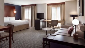 A hotel room with a bed, a desk with a computer, a sofa, a chair, and a TV.