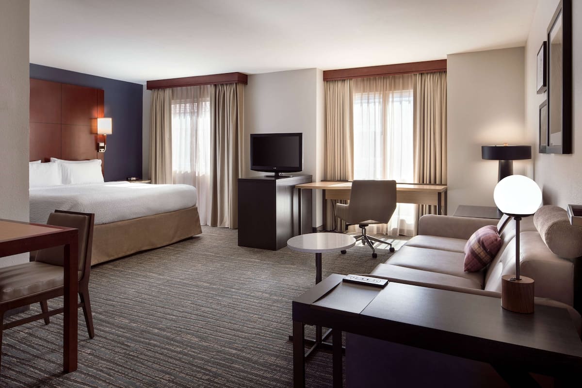 A hotel room with a bed, a desk with a computer, a sofa, a chair, and a TV.