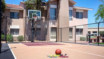 Una cancha de baloncesto al aire libre con un aro de baloncesto, raquetas de tenis y una pelota de tenis.