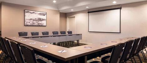 A conference room with a long table, chairs, a projector screen, and a large abstract painting on the wall.