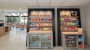 A snack bar with shelves of snacks and a refrigerated display of beverages. - Hampton Inn Seattle/Southcenter (Tukwila)
