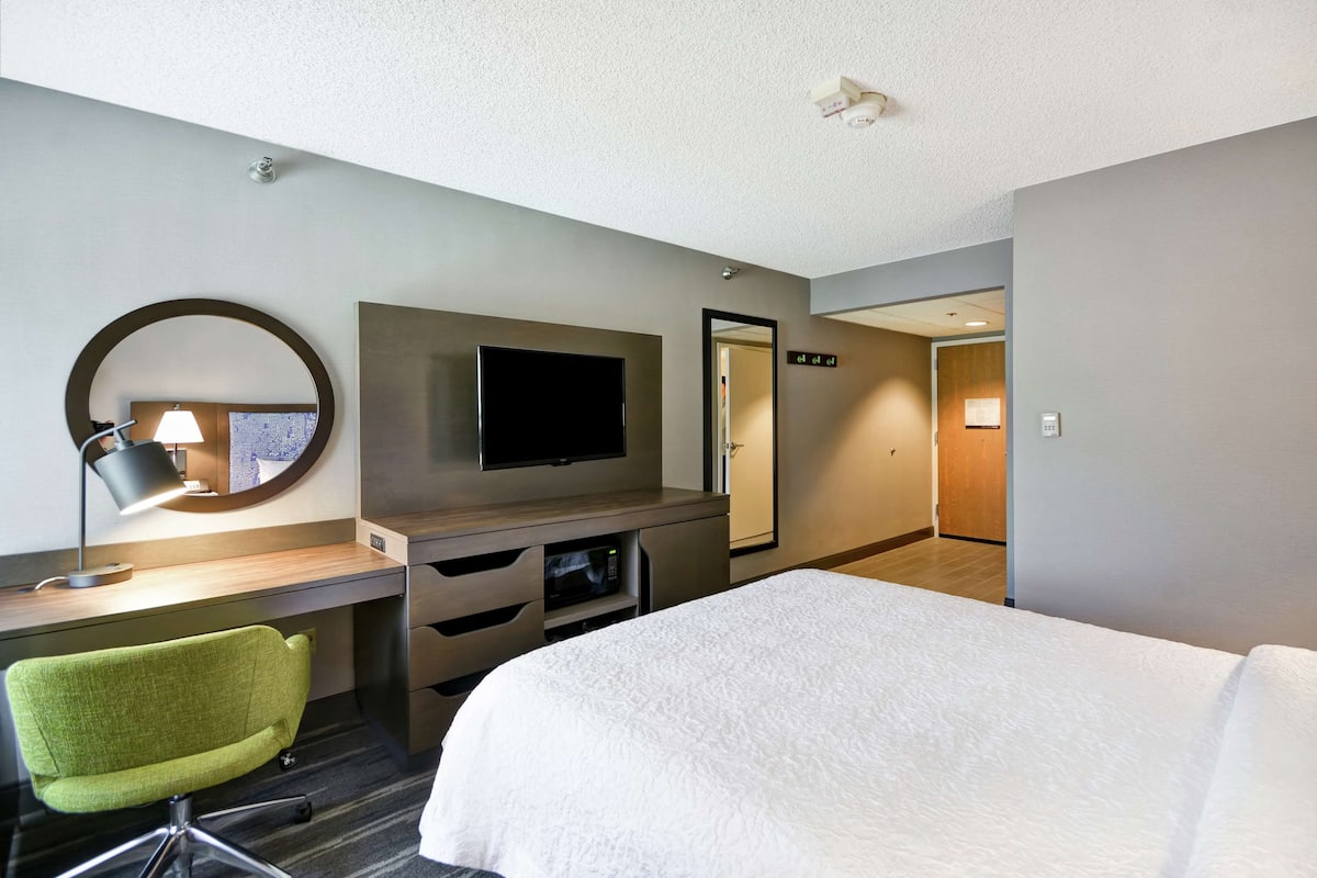 A hotel room with a bed, a desk with a lamp, a TV, a mirror, and a door.
