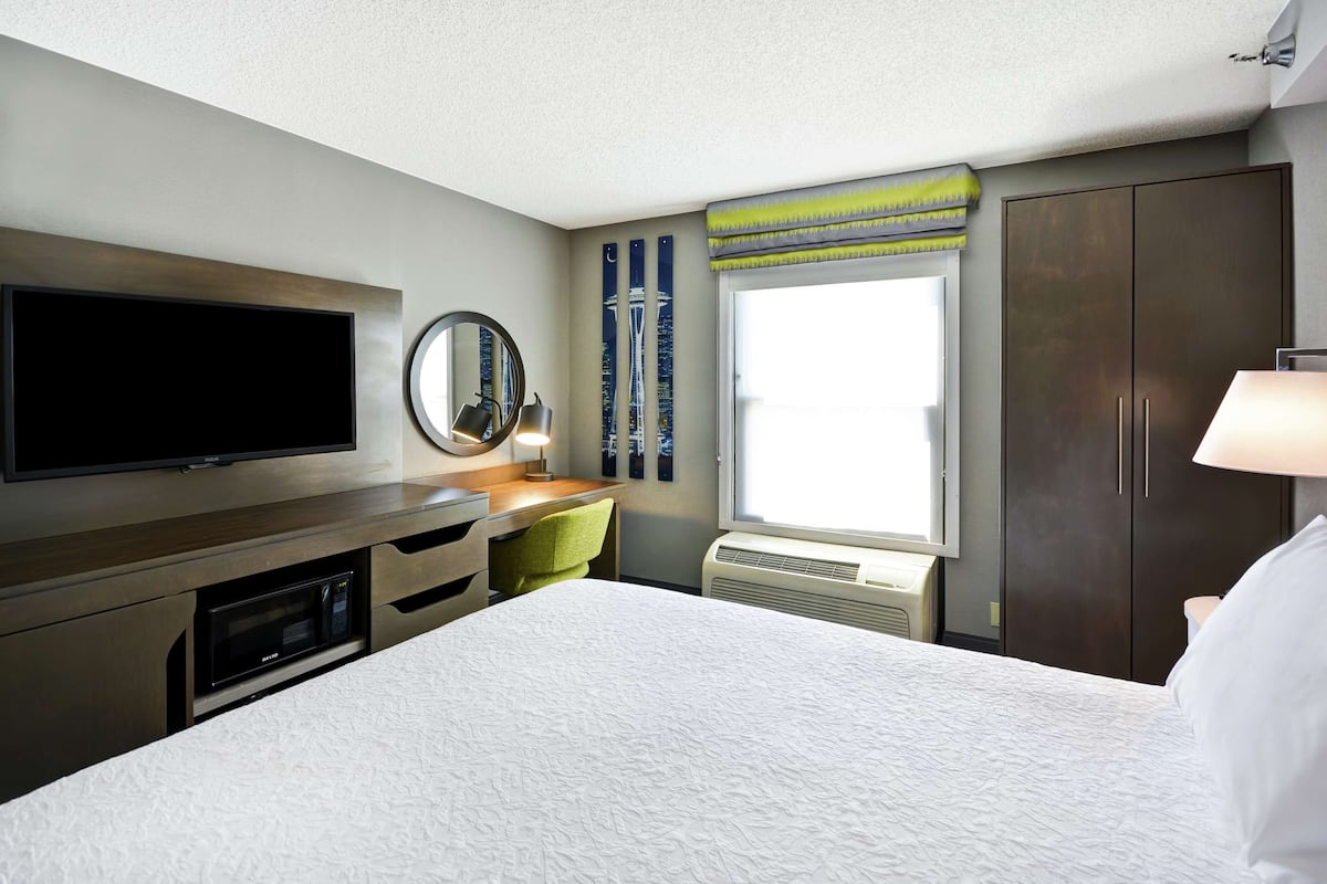 A hotel room with a large bed, a flat-screen TV, a desk with a chair, a window with a view, and a wardrobe.