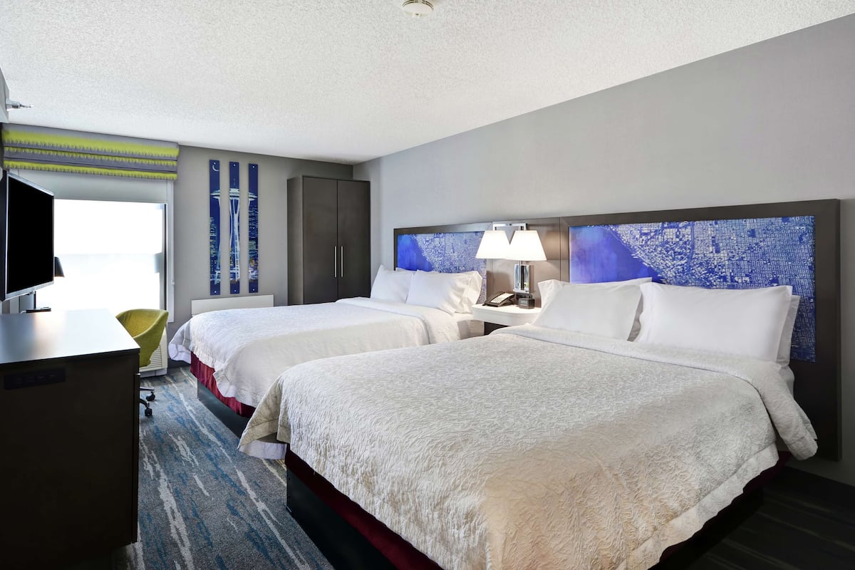 A hotel room with two beds, a desk, a chair, and a large window.
