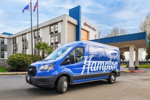 A blue service van with 'Hampton' branding parked in front of a building with a 'Clearance 14' sign.