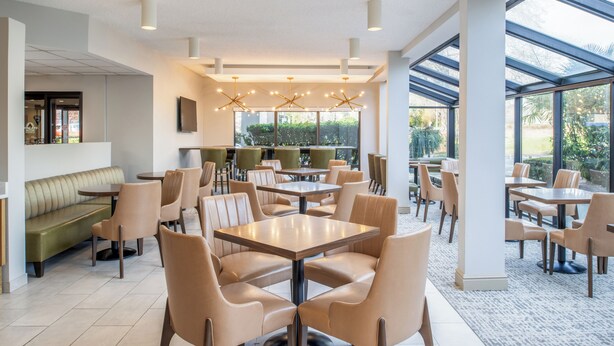 A modern dining area with multiple tables and chairs, a green booth seating area, and large windows providing natural light. - Hampton Inn Seattle/Southcenter (Tukwila)