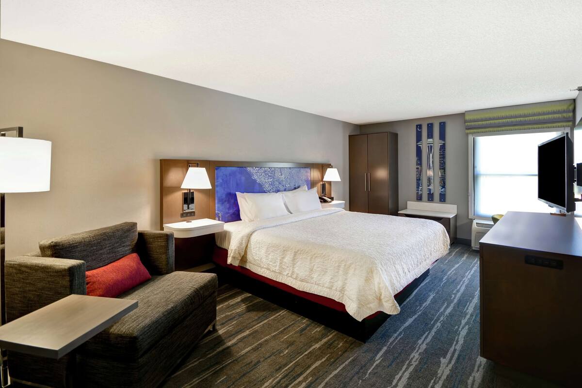 A hotel room with a large bed, a desk, a chair, and a TV.