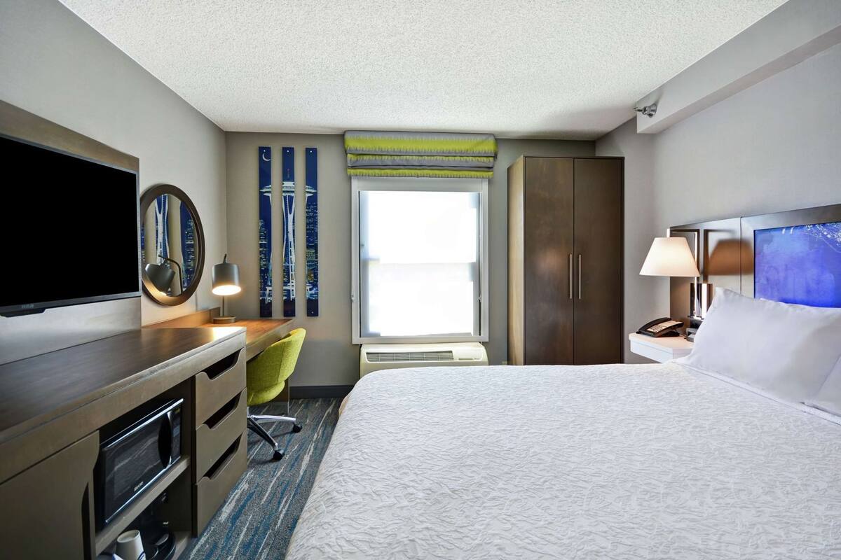 A hotel room with a bed, desk, chair, television, and artwork on the walls.