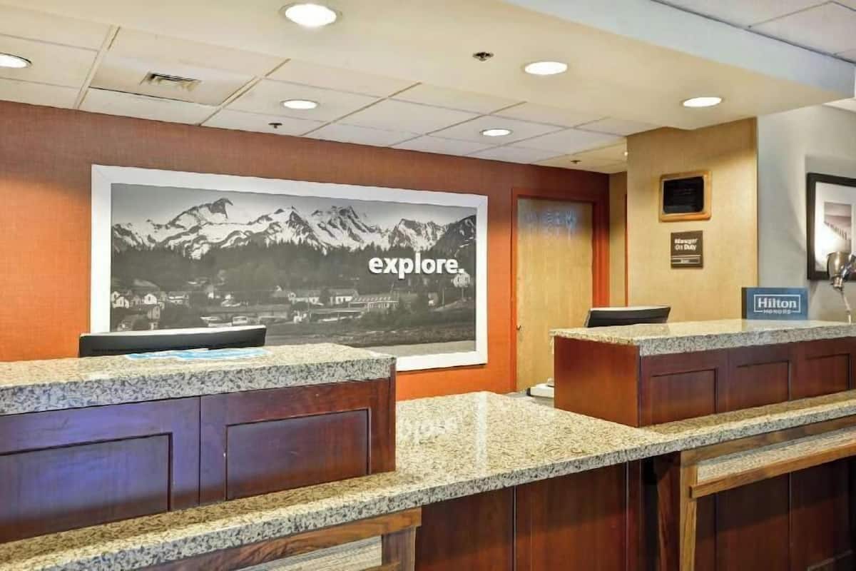 A hotel reception desk with a large 'explore' poster, a wooden reception desk, and a 'Hilton' sign.