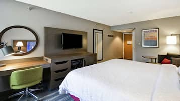 Habitación de hotel con cama, escritorio, silla, televisión y un cuadro en la pared.