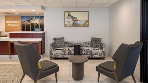 A reception area with a wooden desk, a couch with patterned cushions, two armchairs, and a small round table. - Hampton Inn Seattle/Southcenter (Tukwila)