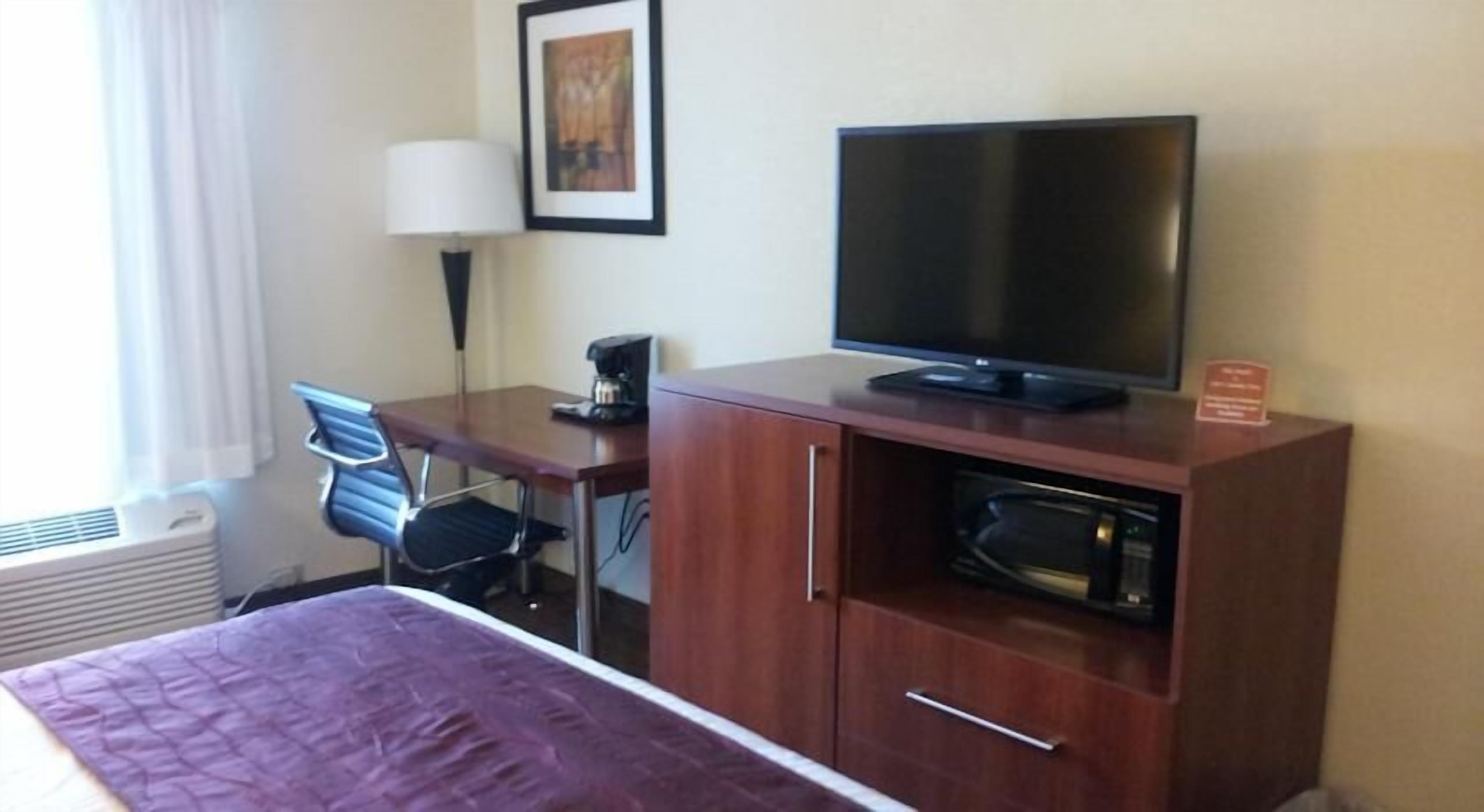 A hotel room with a bed, a desk with a chair, a television, a coffee maker, and a microwave.