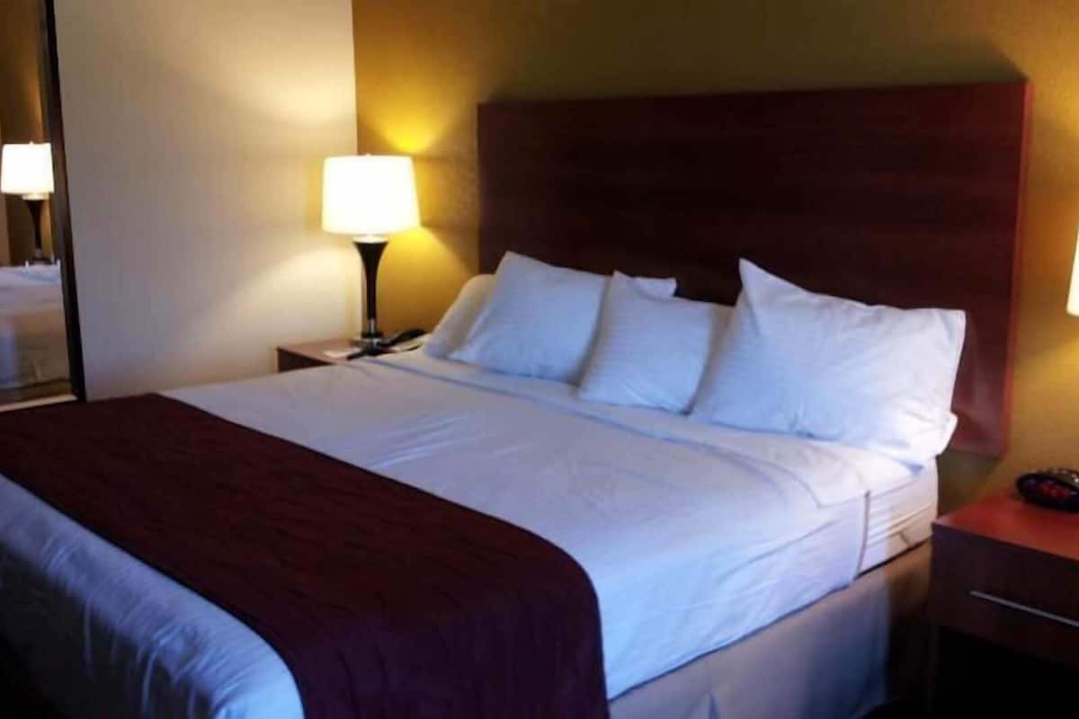 Ein Hotelzimmer mit einem großen Bett, zwei Nachttischlampen, einem Nachttisch und einem Spiegel.