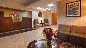 A hotel lobby with a reception desk, seating area, and a vase of flowers on a table.