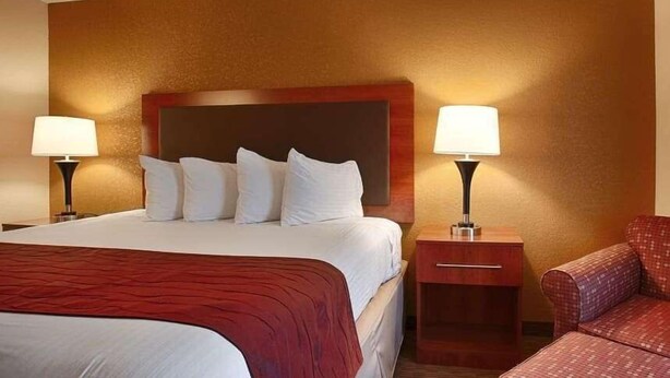 A hotel room with a large bed, two bedside tables, and a red upholstered chair.