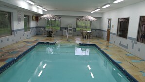 Une piscine dont le fond est recouvert de carrelage, deux tables avec des chaises et des parasols.