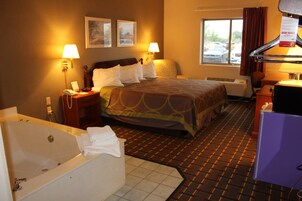 Quarto de hotel com uma cama grande, banheiro separado com banheira, duas luminárias fixadas na parede, janela com vista para carros estacionados e uma escrivaninha com um computador.