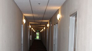 Un long couloir étroit, dont le sol est recouvert de moquette et où l’on trouve des portes de part et d’autre.