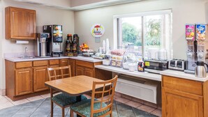 Une cuisine avec des meubles en bois, une table à manger avec des chaises, une machine à café, un grille-pain et une fenêtre donnant sur des arbres.