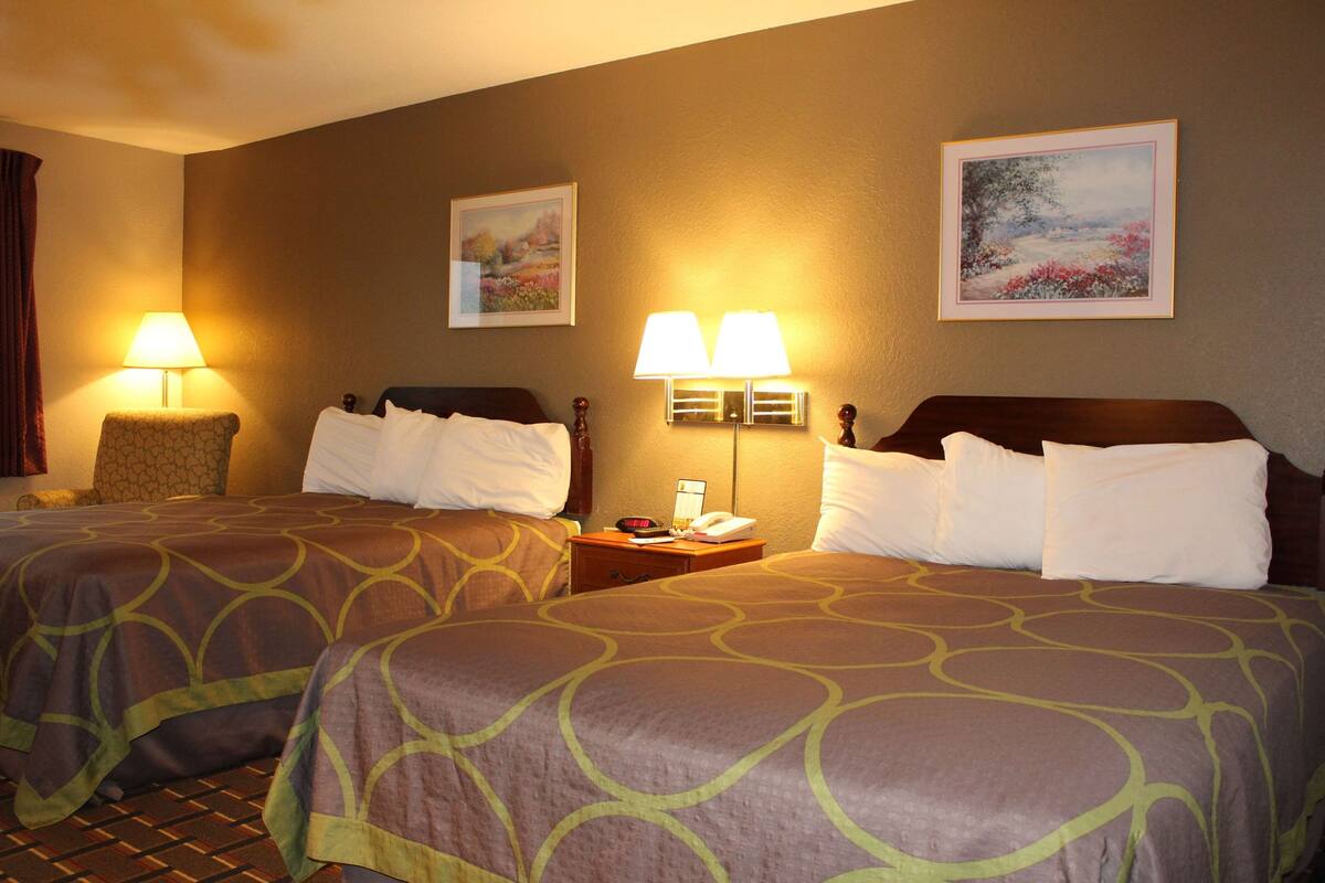 Habitación de hotel con dos camas, cada una con una colcha estampada, una mesita de noche con lámparas y cuadros enmarcados en la pared.