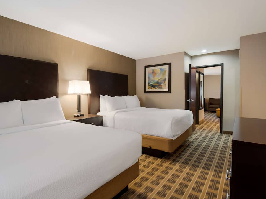 A hotel room with two beds, a nightstand with a lamp, a painting on the wall, and a patterned carpet.