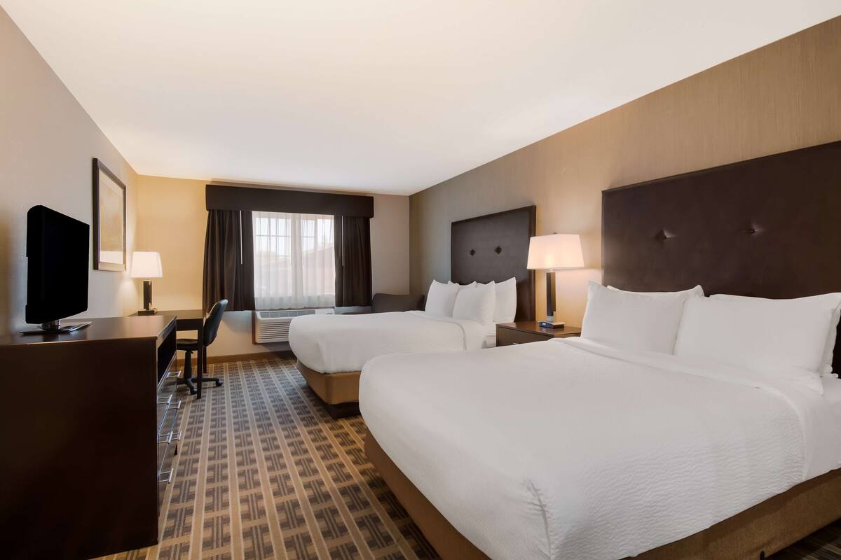 A hotel room with two beds, a desk, a TV, and a window with curtains.