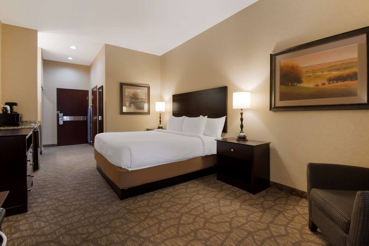 Une chambre d’hôtel avec un grand lit, un bureau avec une machine à café, une chaise et un tableau encadré au mur.