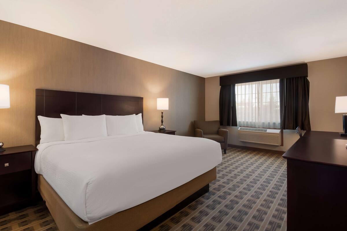 A hotel room with a large bed, two bedside tables, a desk, a chair, and a window with curtains.