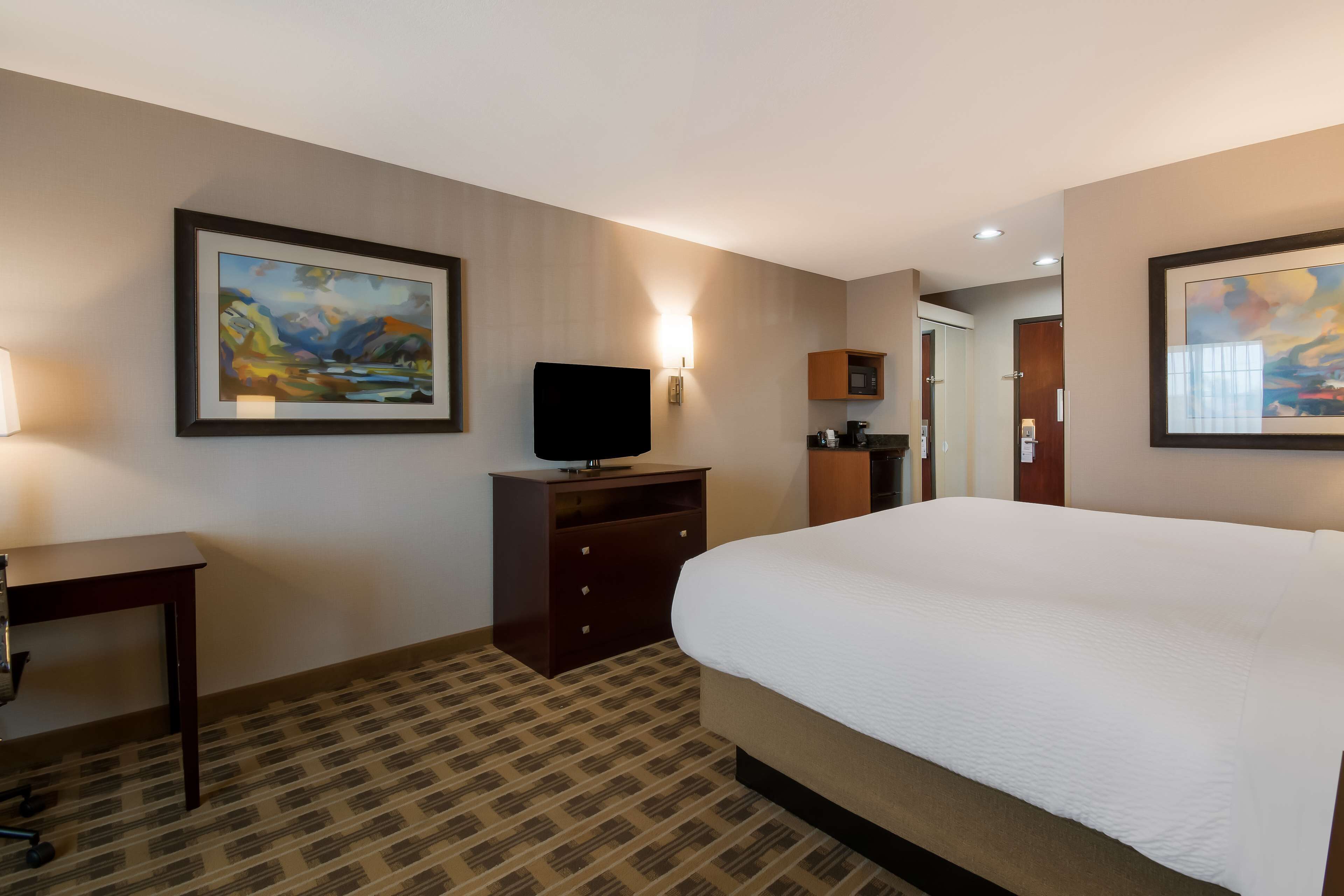 A hotel room with a large bed, a desk, a television, and artwork on the walls.