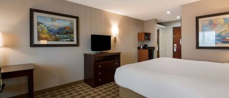 A hotel room with a large bed, a desk, a television, and artwork on the walls.