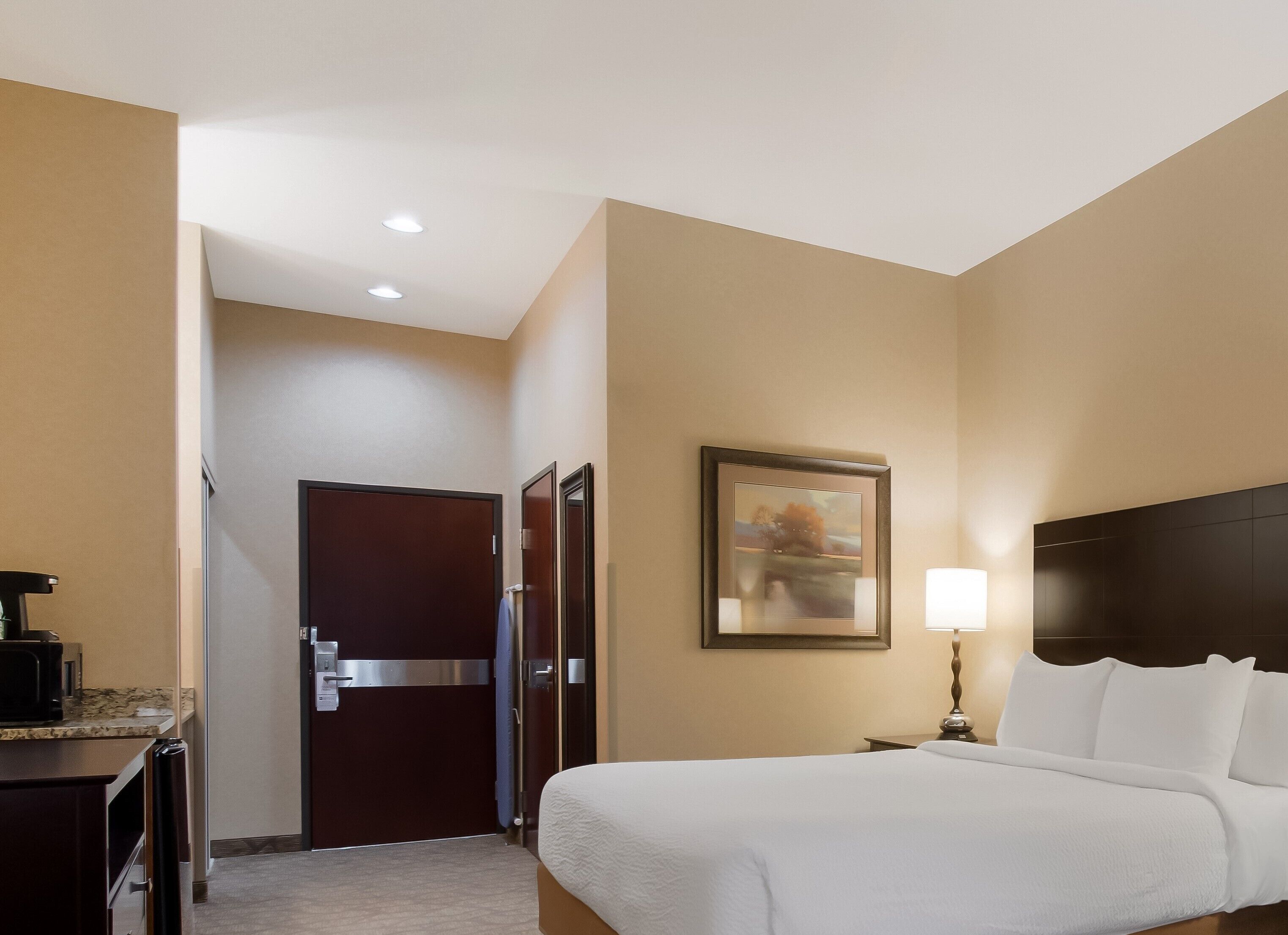 Una camera d'albergo con un letto, una scrivania con una macchina per il caffè, una porta e un quadro appeso al muro.