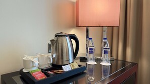 De minibar van een hotelkamer met een koffiezetapparaat, bekers, flessen water en snacks.