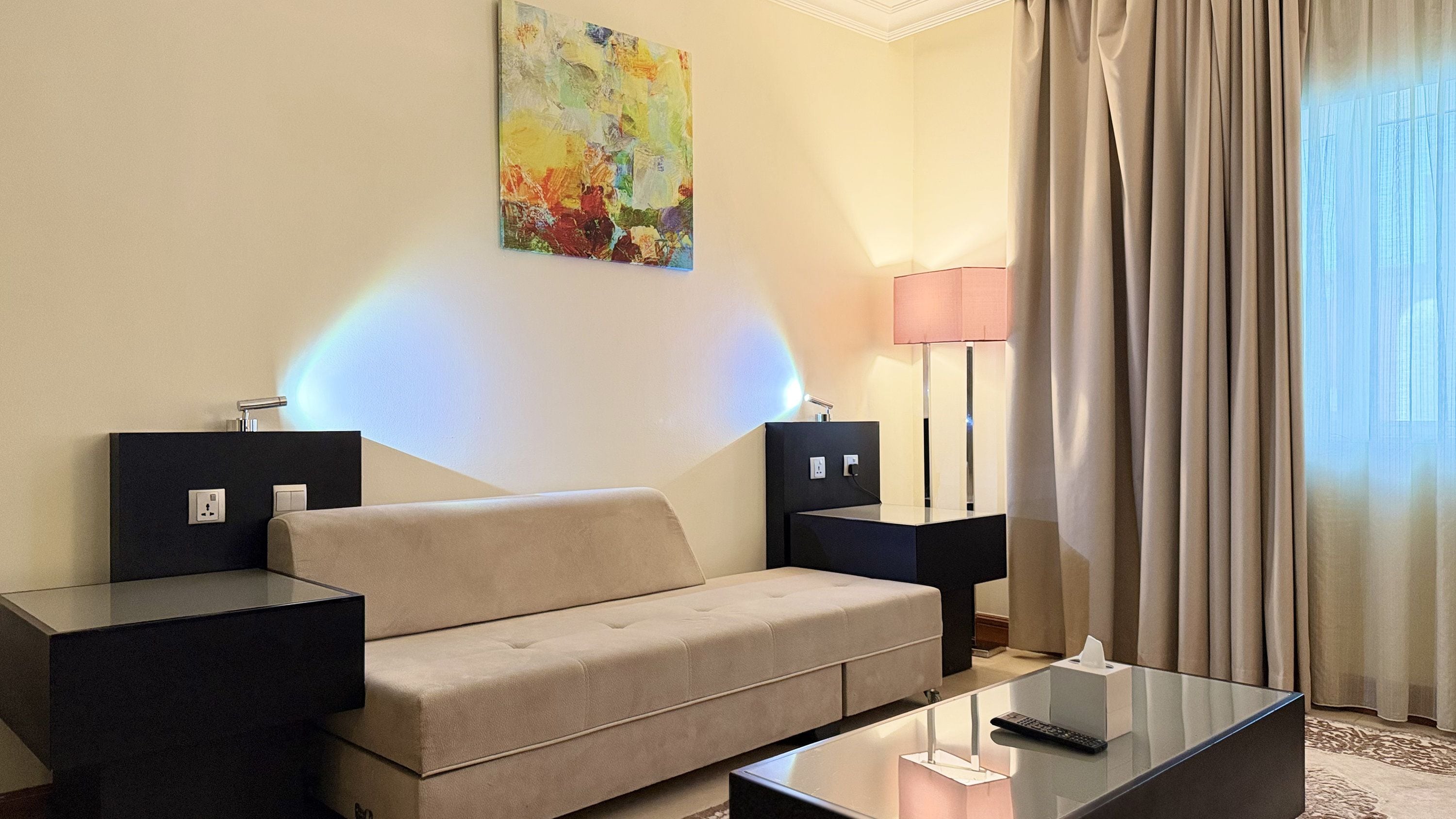 Une chambre d’hôtel avec un canapé, une table basse en verre, une lampe et un tableau au mur.