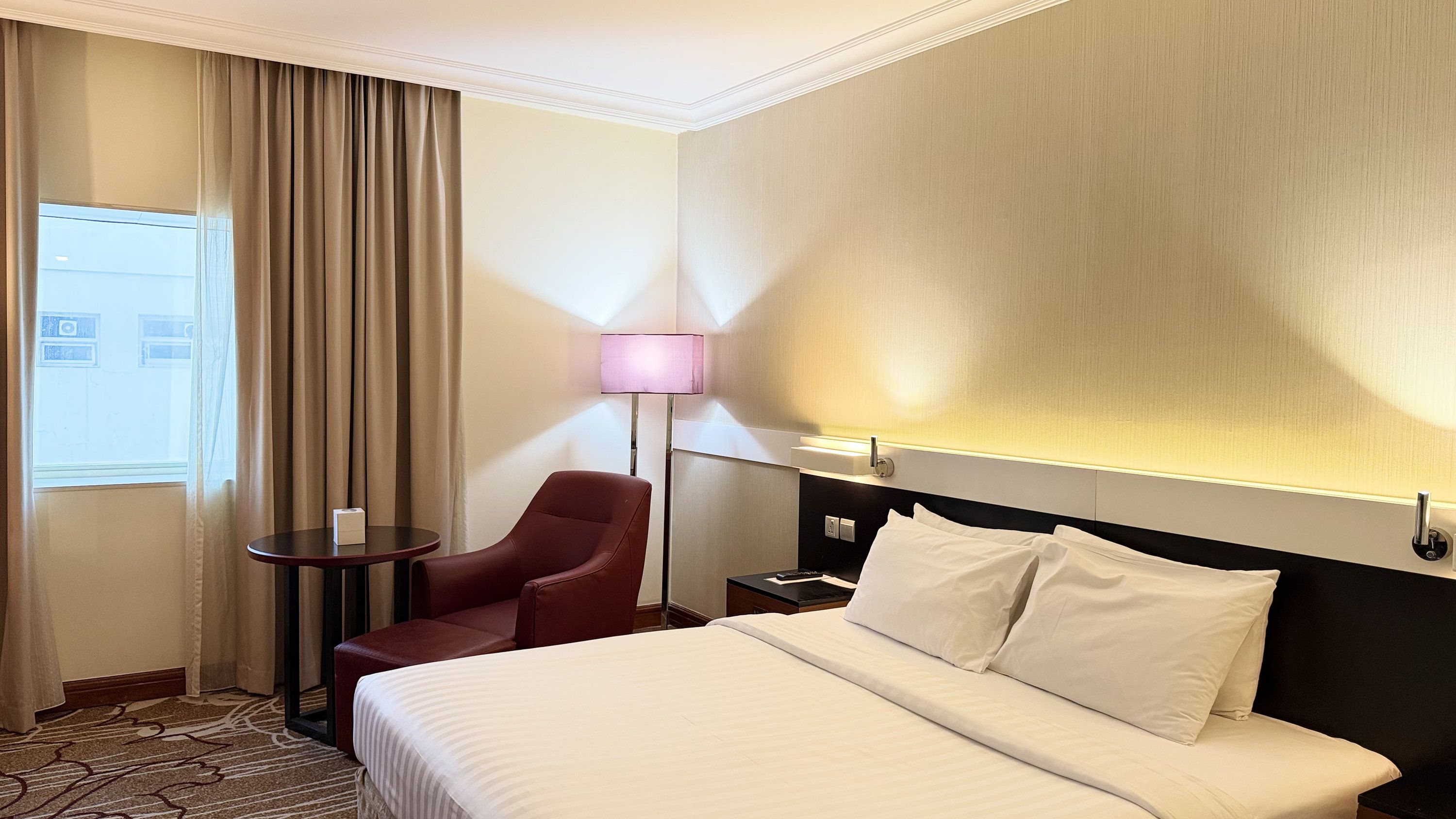 A hotel room with a bed, a chair, a table, and a lamp.