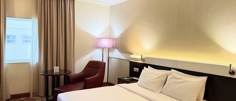 A hotel room with a bed, a chair, a table, and a lamp.