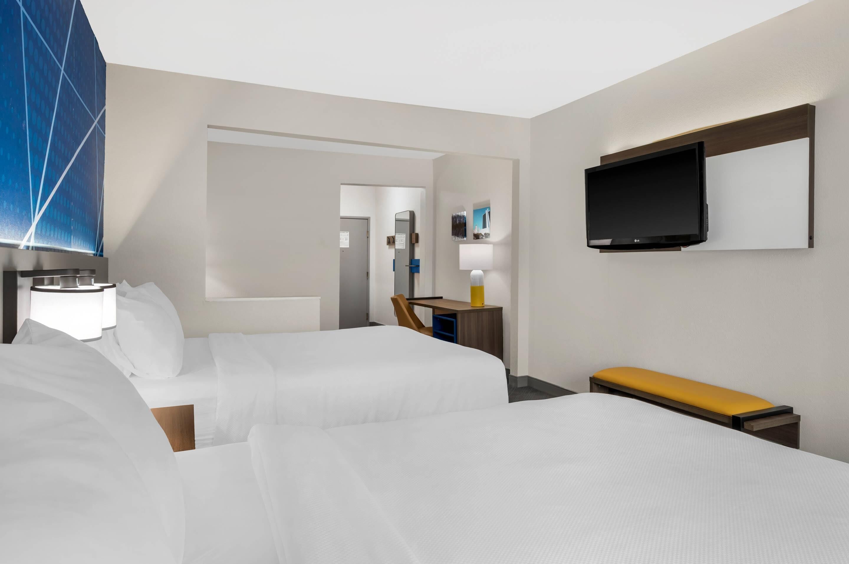 A hotel room with two beds, a desk, a television, and a bathroom visible through an open door.