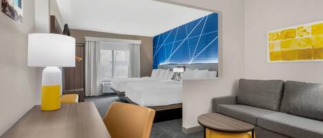 Una camera d'albergo con un letto, un divano, un tavolo da pranzo, una lampada e un quadro appeso al muro.