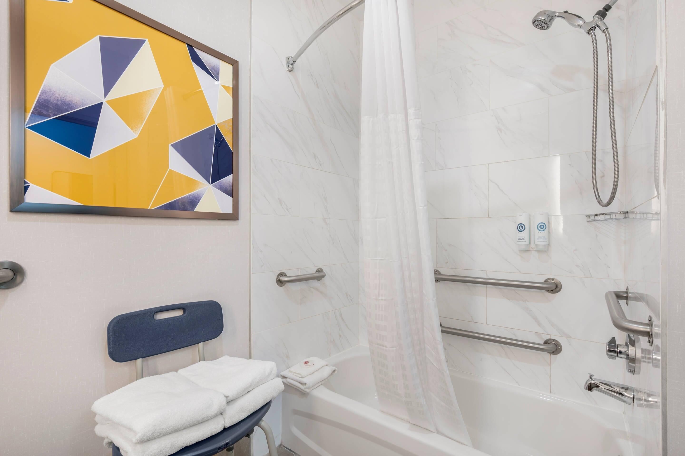 A bathroom with a shower, a handrail, a towel rack, and a wall-mounted artwork.