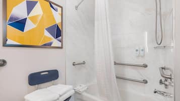 A bathroom with a shower, a handrail, a towel rack, and a wall-mounted artwork.