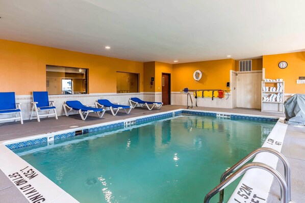 Une piscine intérieure avec des chaises longues bleues, une horloge au mur et un panneau indiquant une profondeur de 1,52 mètre pour la plongée.